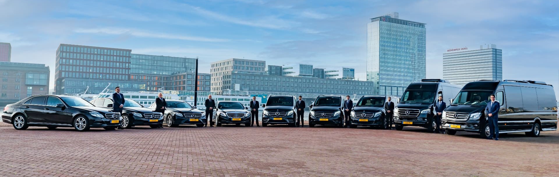 CSH chauffeurs in suits beside a lineup of black Mercedes-Benz sedans and vans